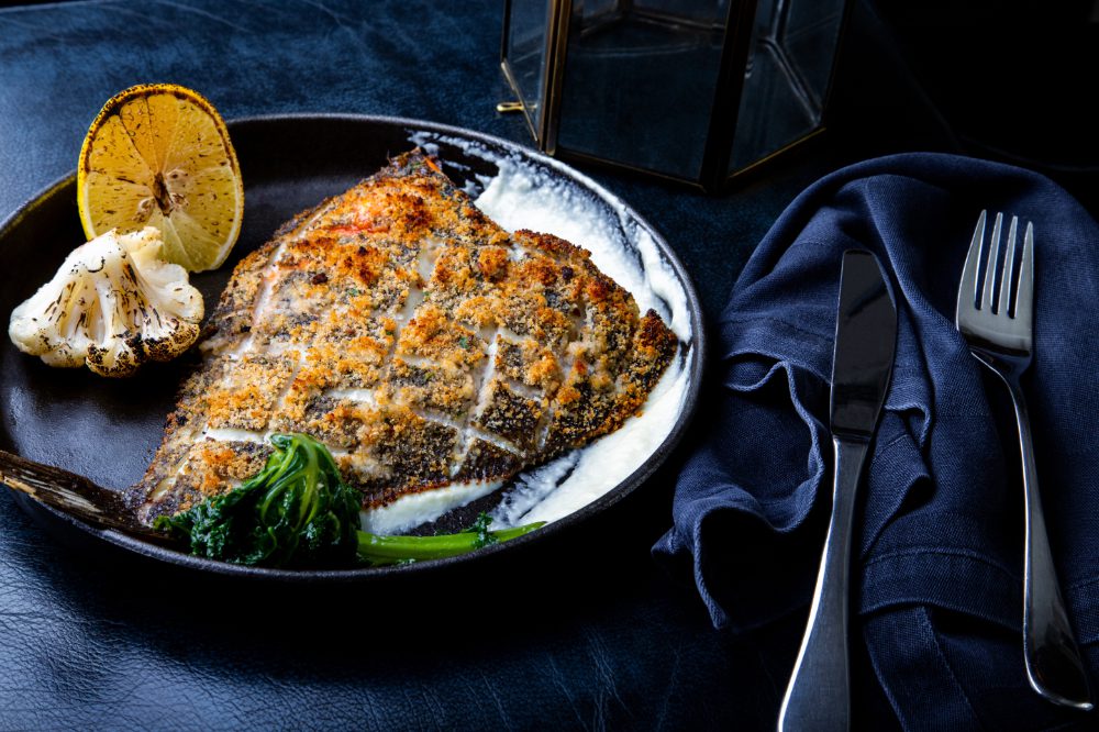 Crumbed fish fillet with roasted vegetables and lemon on a plate with cutlery